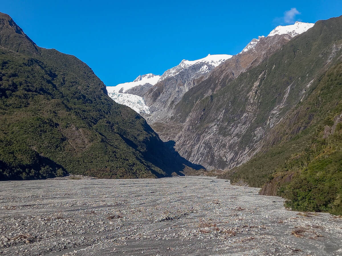 View of riverbed and Franz Josef Glacier surrounded by snow covered moutains.